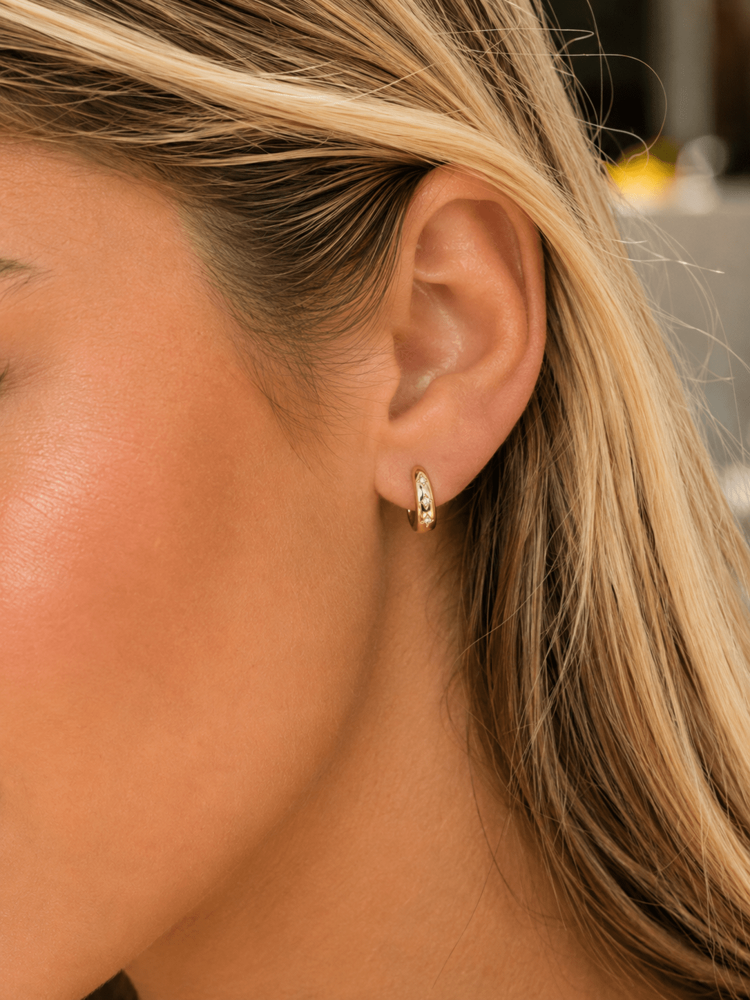 Close-up of a woman's ear wearing a small gold crystal hoop earring.