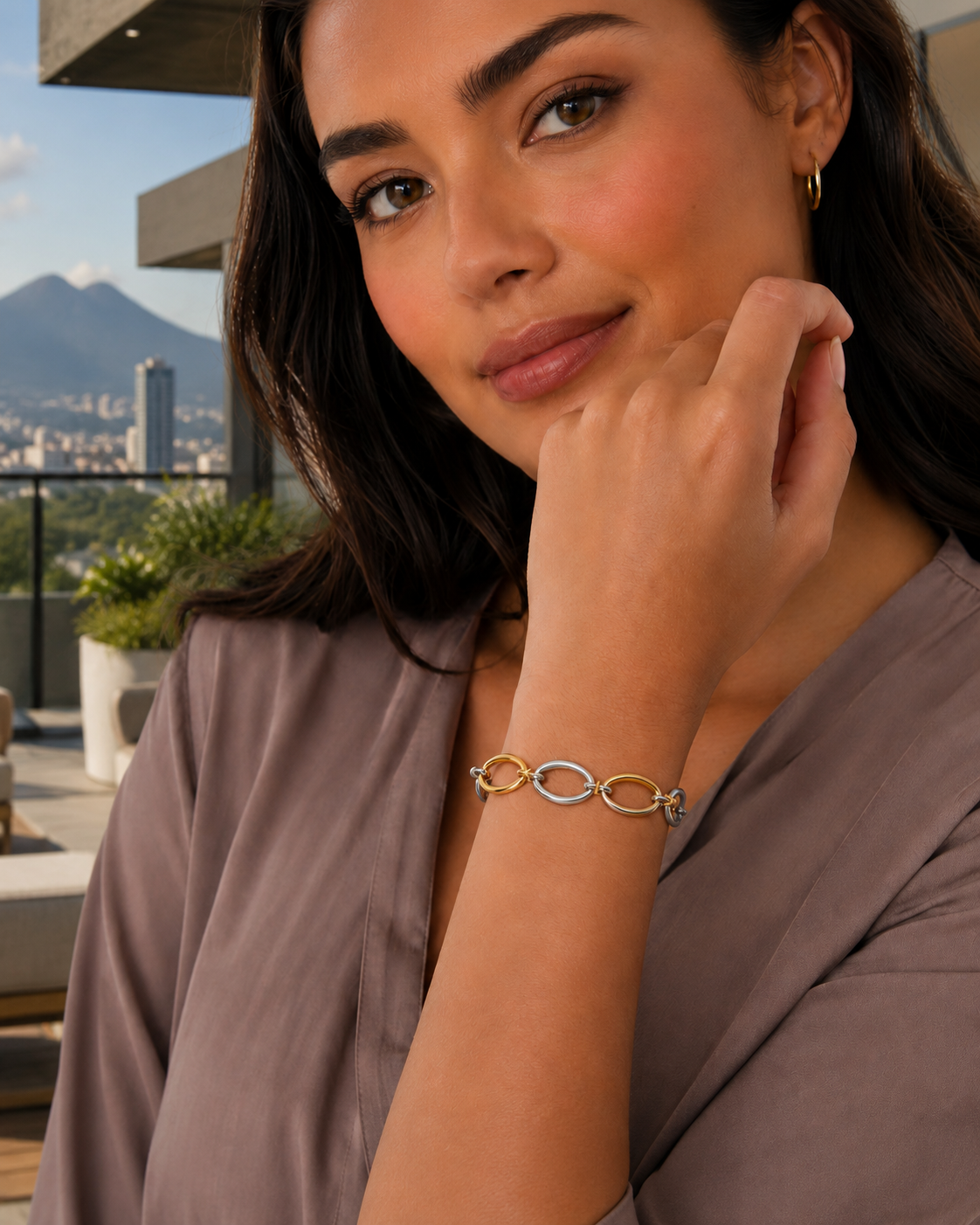 A woman wearing the Cora Two-Tone Oval Link Bracelet, with a city skyline in the background.