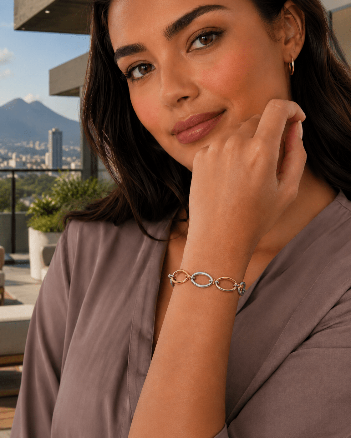 A woman wearing the Cora Two-Tone Oval Link Bracelet, with a city skyline in the background.
