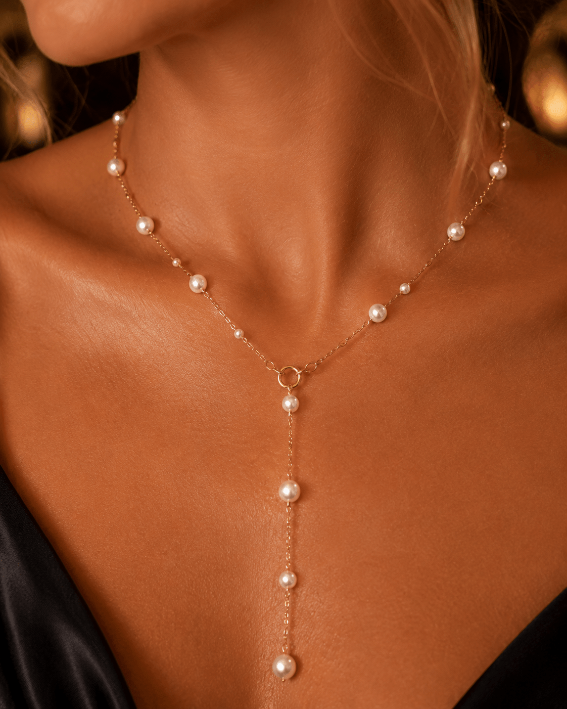 A delicate gold Y-necklace with small white pearls, worn on a model's neck and upper chest.