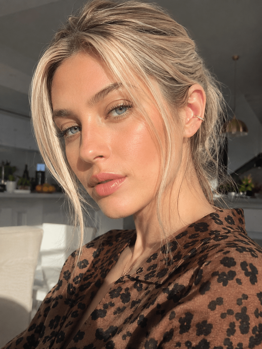 A woman wearing a gold crystal C-cuff earring, close-up selfie-style portrait.