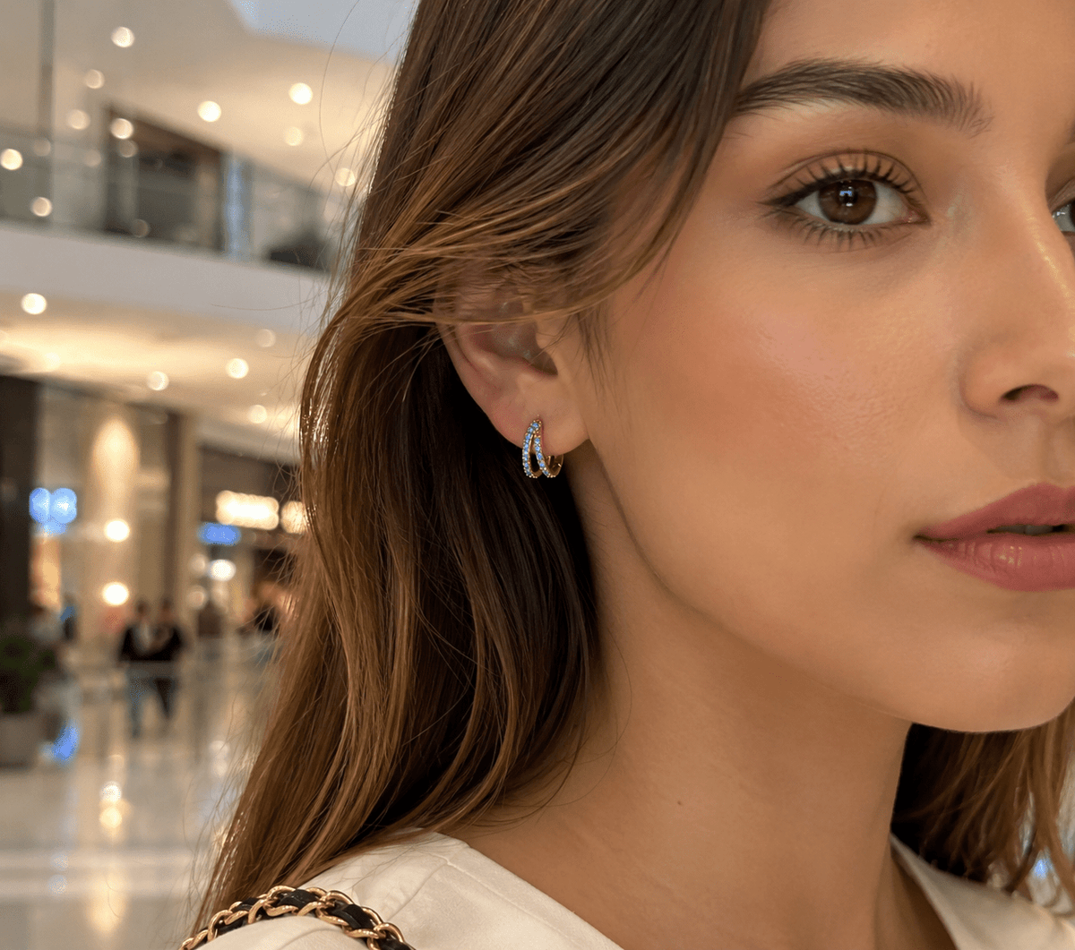 Woman wearing Marina gold hoop earrings with an aqua crystal bar accent