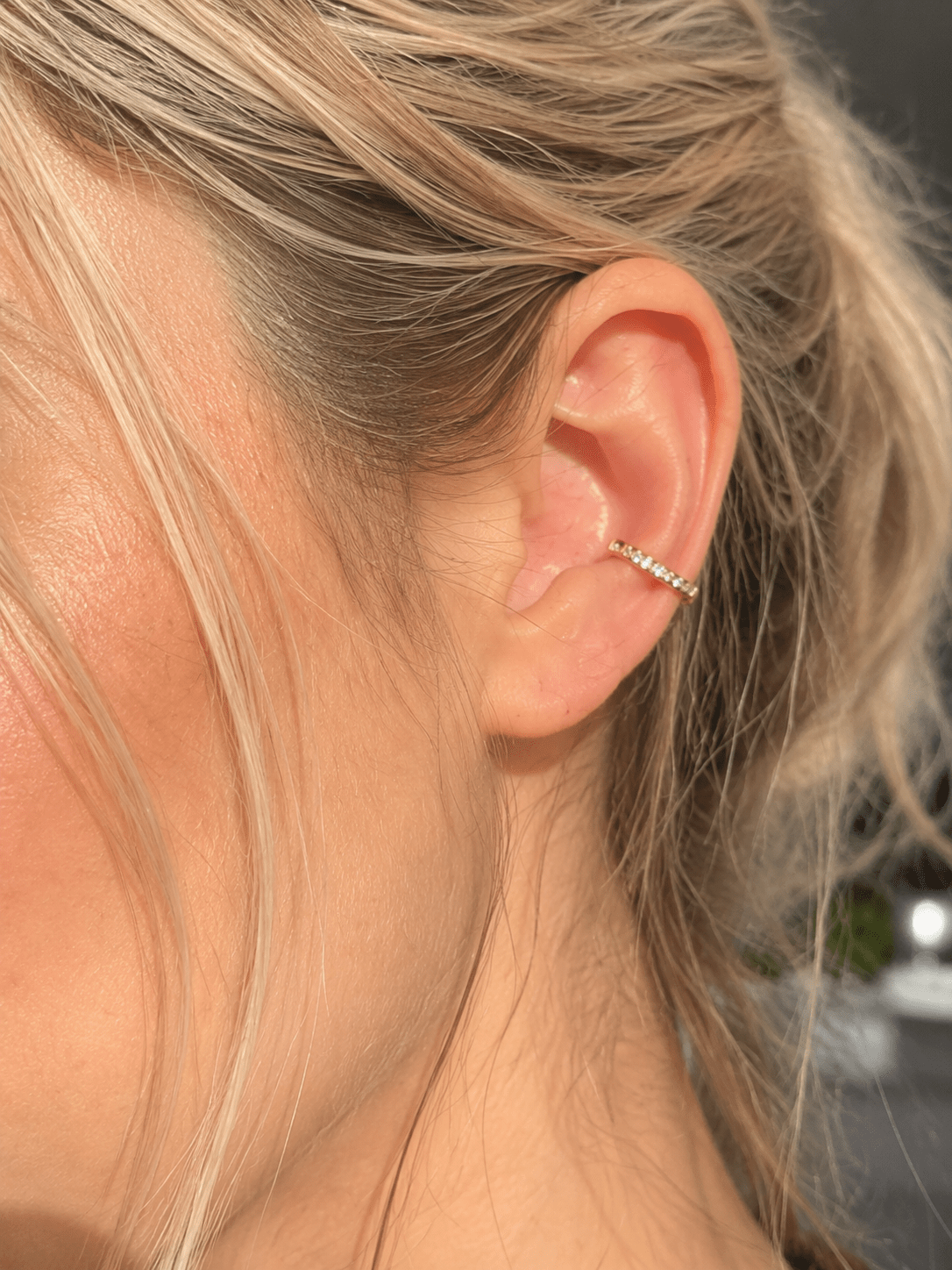Close-up of a woman's ear wearing a gold crystal C-cuff earring.