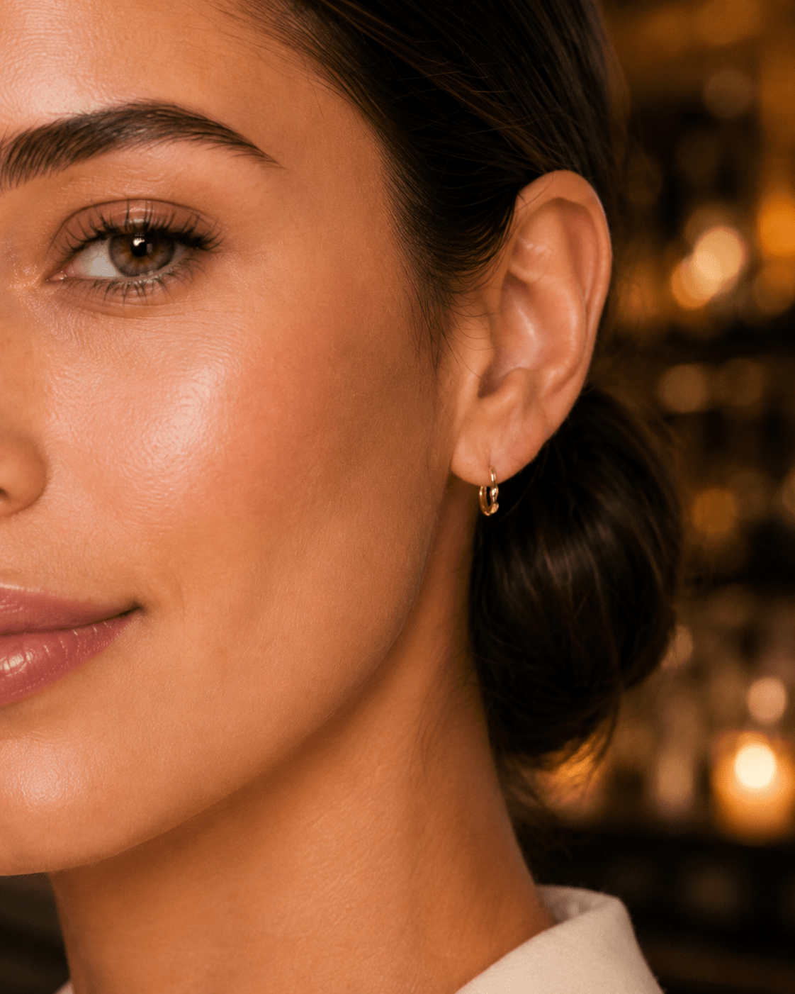 Close-up of a woman's ear wearing a small gold hoop earring.