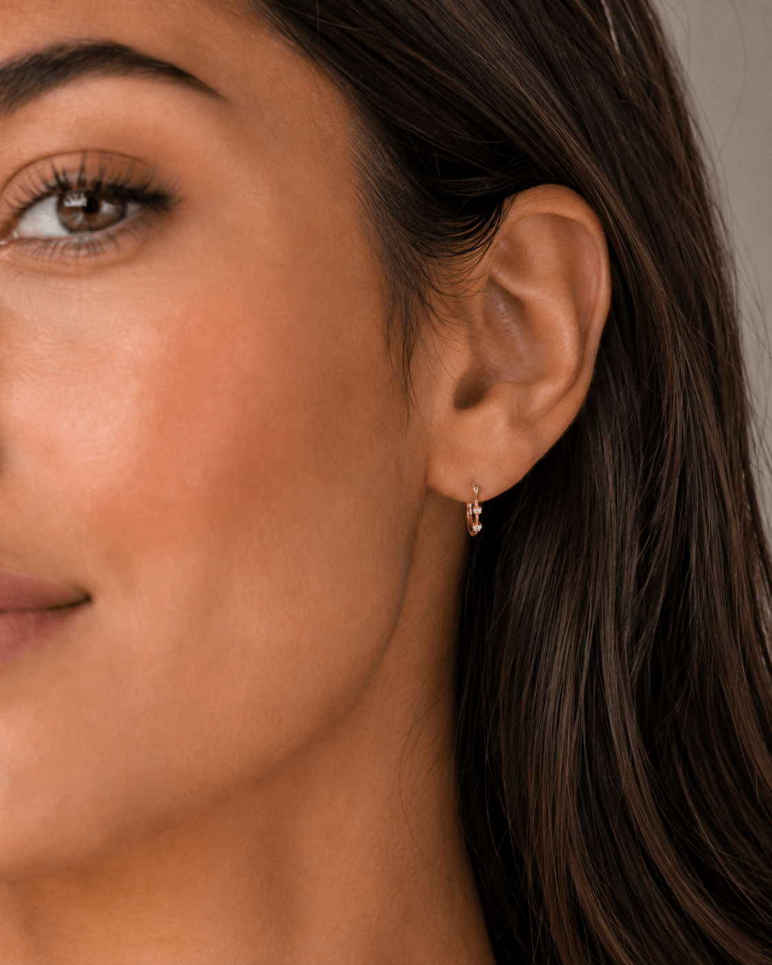 Close-up of a woman's ear wearing a small gold crystal huggie hoop earring.